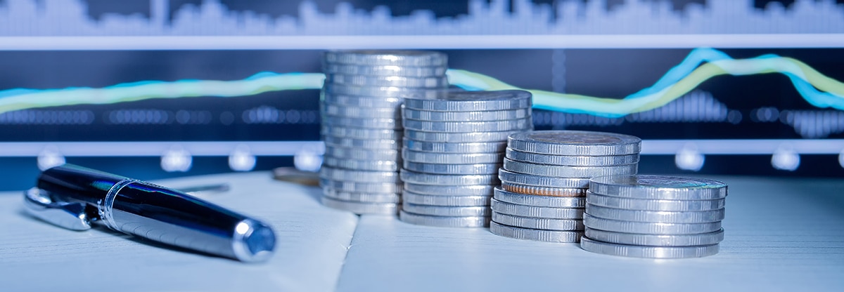 Image of coins and a pen in front of a computer showing a graph.